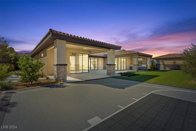 back of property with stone siding, stucco siding, a tiled roof, and a lawn