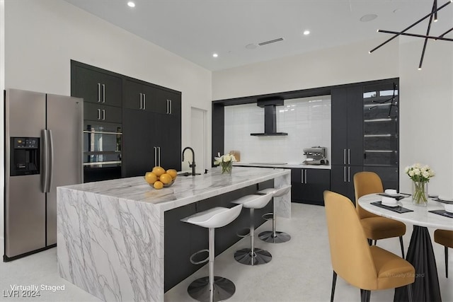 kitchen with wall chimney exhaust hood, modern cabinets, dark cabinetry, and stainless steel refrigerator with ice dispenser