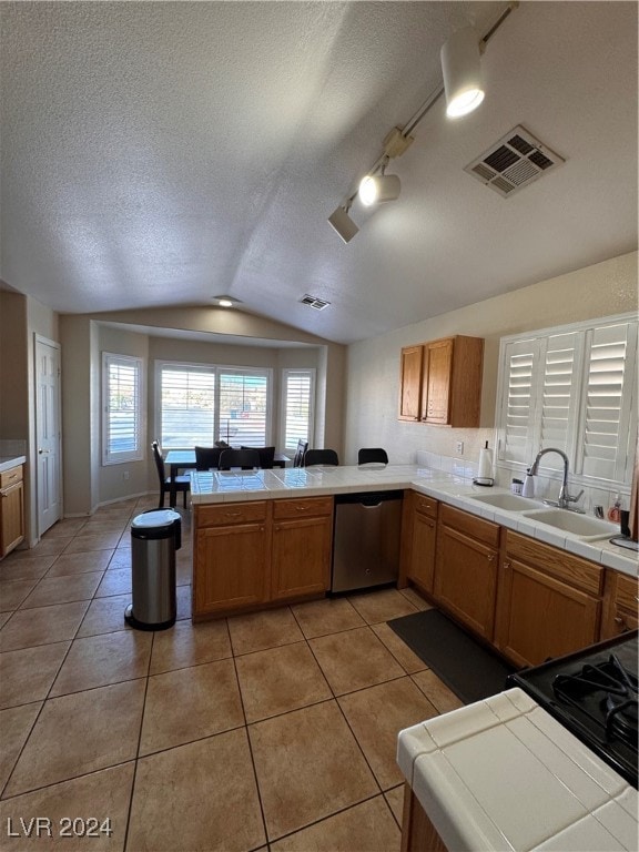 kitchen featuring sink, tile counters, stainless steel dishwasher, kitchen peninsula, and lofted ceiling