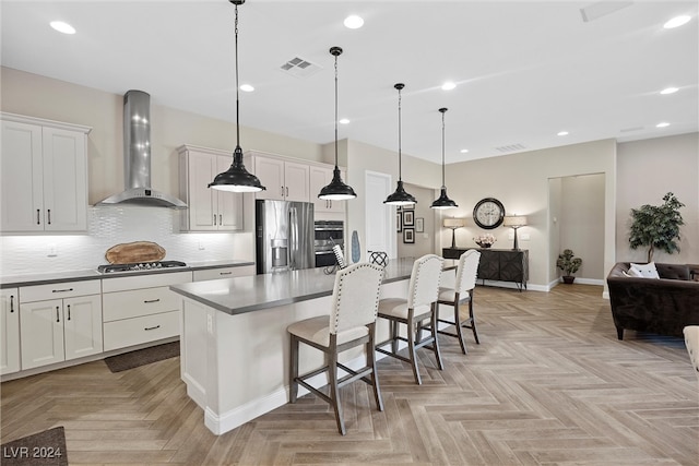 kitchen with pendant lighting, white cabinets, a kitchen breakfast bar, wall chimney range hood, and stainless steel appliances