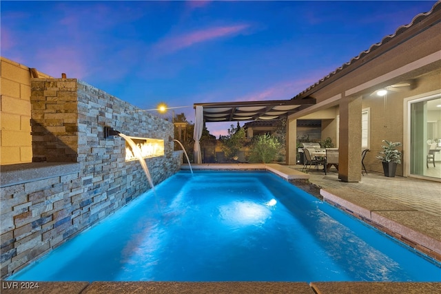 pool at dusk featuring pool water feature, ceiling fan, and a patio