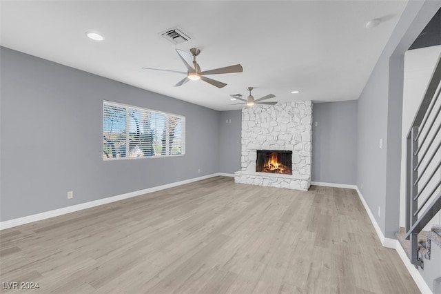 unfurnished living room featuring a stone fireplace, ceiling fan, and light hardwood / wood-style flooring