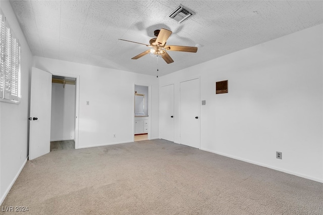 unfurnished bedroom with ceiling fan, ensuite bath, a textured ceiling, and carpet