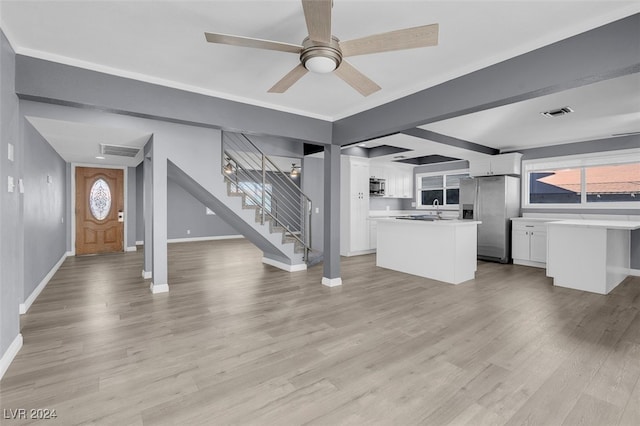 unfurnished living room with ceiling fan, beamed ceiling, sink, and light hardwood / wood-style flooring