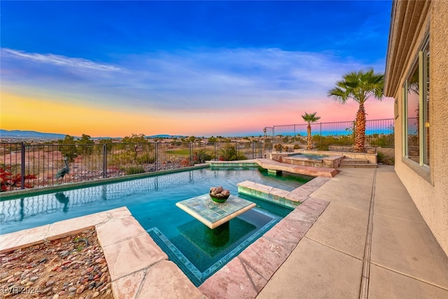 pool at dusk with a patio area and an in ground hot tub