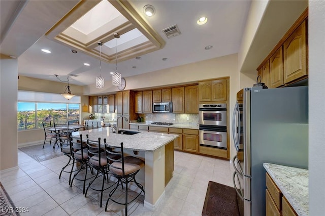 kitchen featuring a breakfast bar, a center island with sink, stainless steel appliances, visible vents, and light stone countertops