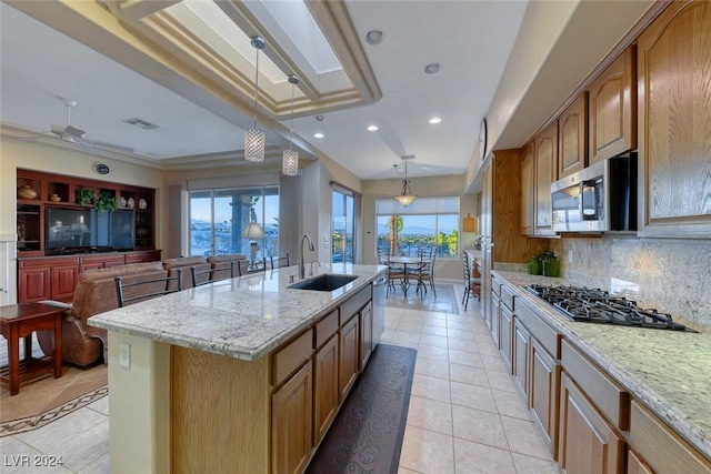 kitchen with light stone counters, pendant lighting, appliances with stainless steel finishes, a sink, and an island with sink