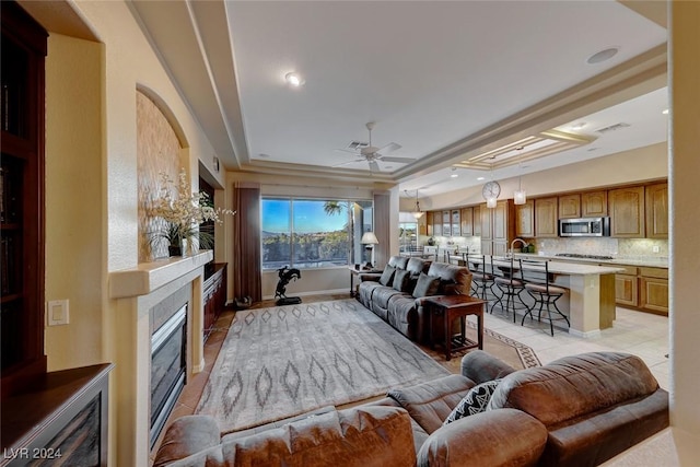 living area with visible vents, a tray ceiling, a ceiling fan, and light tile patterned flooring