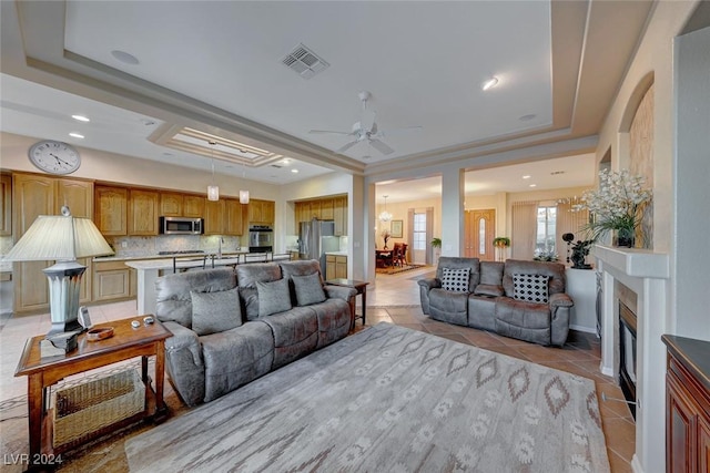 living area with light tile patterned floors, a raised ceiling, visible vents, a fireplace with flush hearth, and ceiling fan