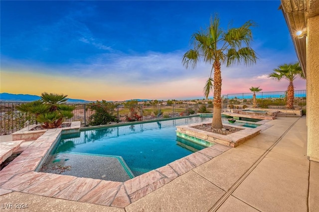 pool at dusk with a fenced in pool, a fenced backyard, a patio, and an in ground hot tub