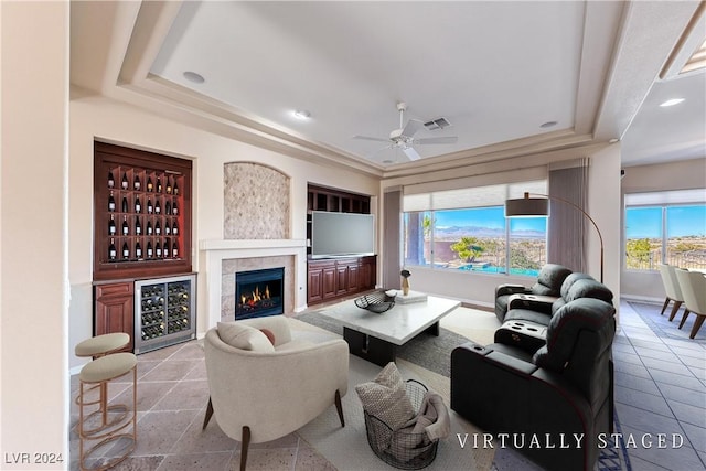 living room featuring visible vents, baseboards, a tiled fireplace, ceiling fan, and a tray ceiling