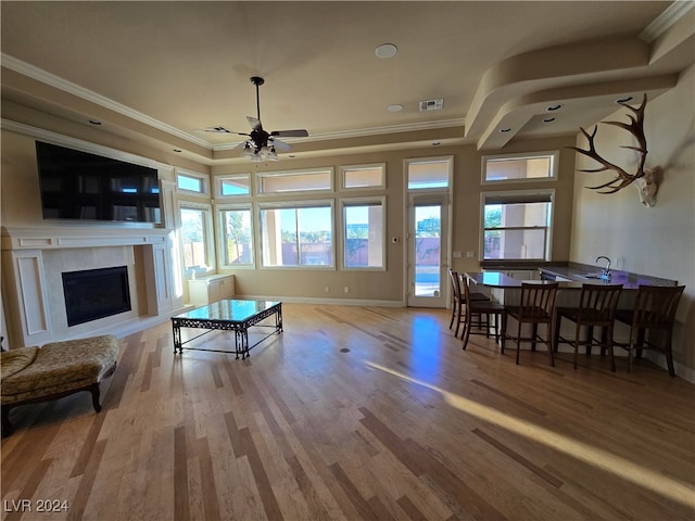 living room featuring ceiling fan, a tray ceiling, crown molding, and light hardwood / wood-style flooring