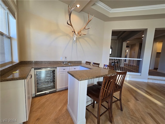 kitchen featuring wine cooler, kitchen peninsula, light hardwood / wood-style floors, and white cabinets