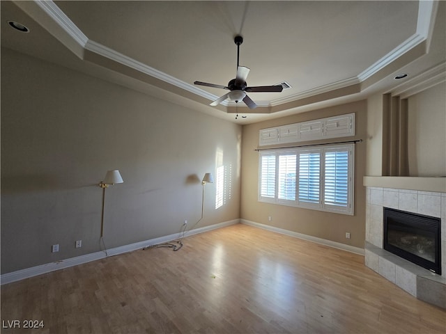 unfurnished living room featuring a tiled fireplace, ornamental molding, light wood-type flooring, and a tray ceiling