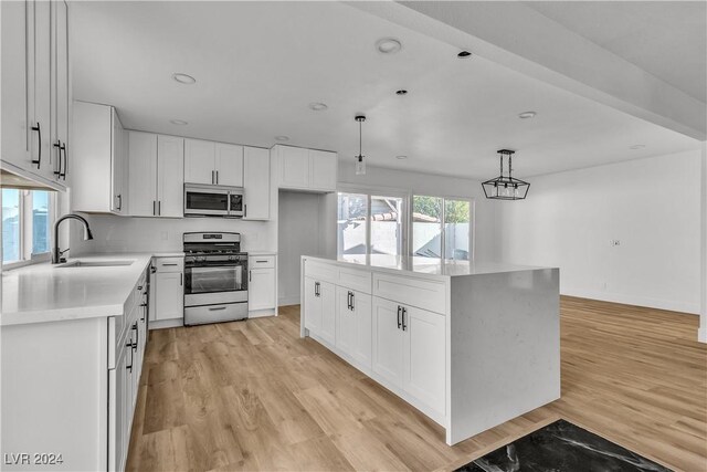 kitchen with appliances with stainless steel finishes, light wood-type flooring, sink, white cabinetry, and hanging light fixtures