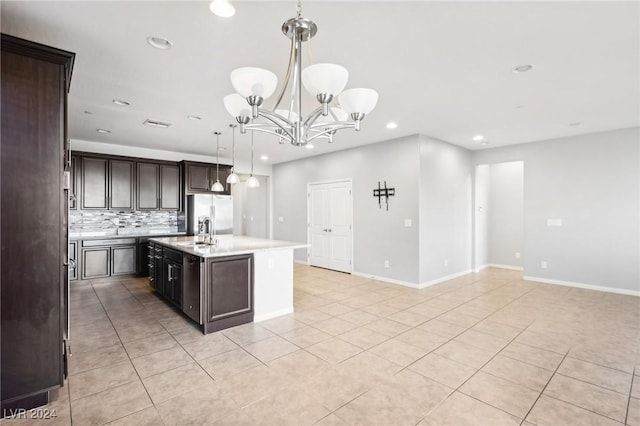 kitchen featuring a kitchen island with sink, sink, hanging light fixtures, decorative backsplash, and dark brown cabinetry