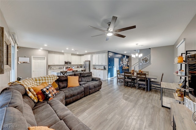 living room featuring ceiling fan with notable chandelier and light hardwood / wood-style flooring