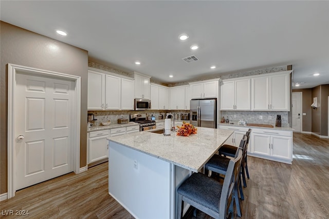 kitchen featuring stainless steel appliances, light hardwood / wood-style floors, white cabinetry, and an island with sink