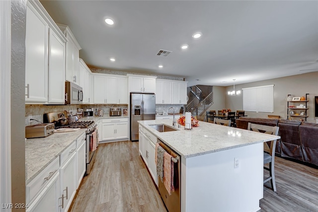 kitchen featuring light hardwood / wood-style floors, a center island with sink, sink, light stone counters, and appliances with stainless steel finishes