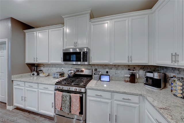 kitchen featuring backsplash, light stone countertops, white cabinetry, light wood-type flooring, and appliances with stainless steel finishes