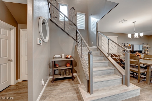 stairway with wood-type flooring and an inviting chandelier