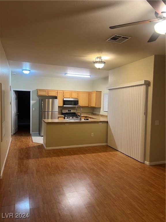 kitchen with wood-type flooring, kitchen peninsula, ceiling fan, appliances with stainless steel finishes, and light brown cabinetry