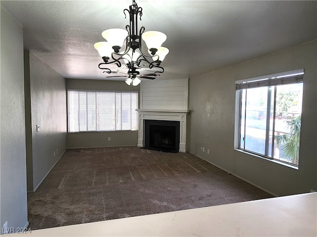 unfurnished living room with ceiling fan with notable chandelier, a textured ceiling, dark colored carpet, and a fireplace