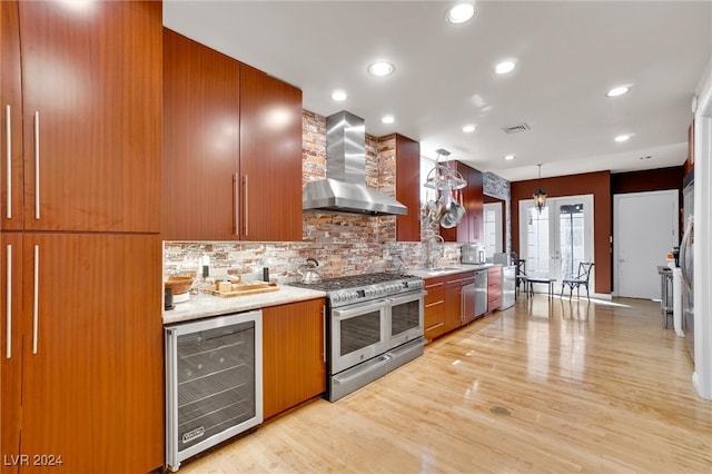 kitchen with stainless steel appliances, light wood-type flooring, wall chimney range hood, decorative light fixtures, and beverage cooler