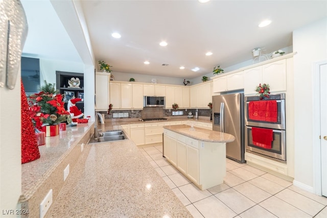 kitchen with a center island, light stone counters, decorative backsplash, sink, and appliances with stainless steel finishes