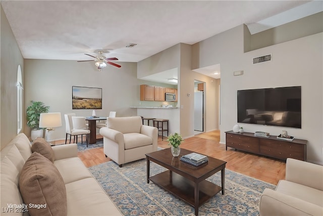 living room with ceiling fan, light wood-type flooring, and high vaulted ceiling