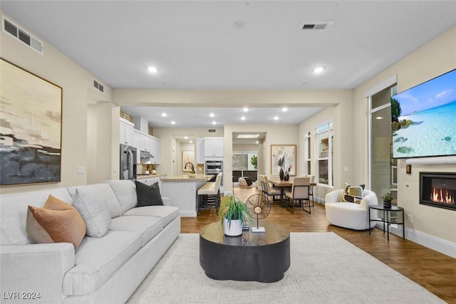 living area featuring wood finished floors, a glass covered fireplace, and visible vents