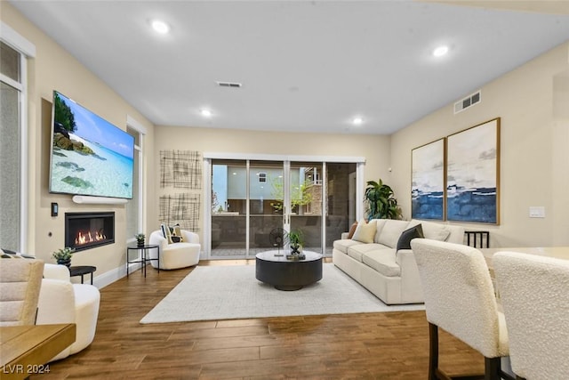 living area featuring a glass covered fireplace, visible vents, recessed lighting, and wood finished floors