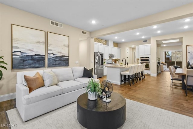 living room with light wood finished floors, baseboards, visible vents, and recessed lighting