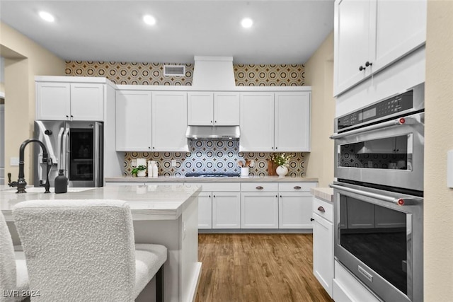 kitchen with appliances with stainless steel finishes, backsplash, white cabinetry, and under cabinet range hood