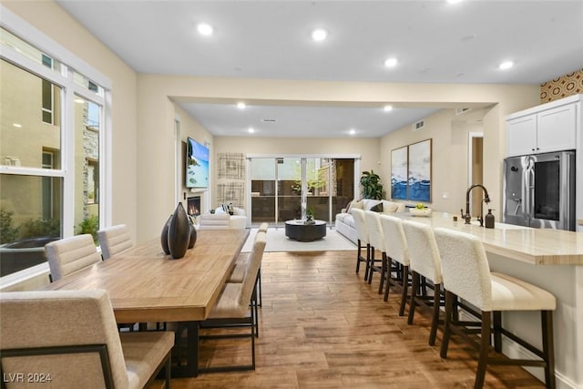 kitchen with stainless steel fridge, open floor plan, wood finished floors, a lit fireplace, and a kitchen bar