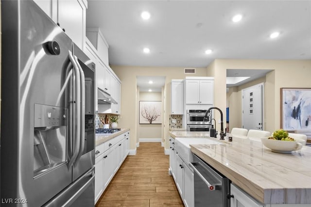 kitchen featuring backsplash, appliances with stainless steel finishes, white cabinets, an island with sink, and under cabinet range hood