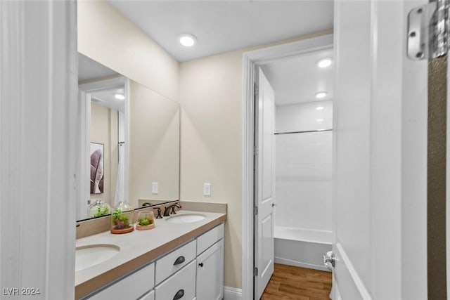 bathroom with shower / bathtub combination, double vanity, wood finished floors, and a sink