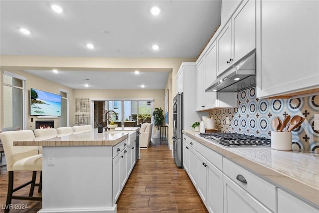 kitchen featuring dark wood finished floors, stainless steel appliances, open floor plan, under cabinet range hood, and a kitchen bar