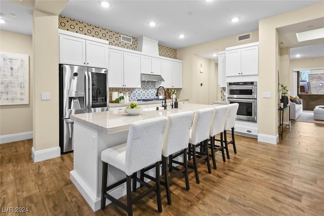 kitchen featuring a center island with sink, a breakfast bar area, visible vents, appliances with stainless steel finishes, and under cabinet range hood