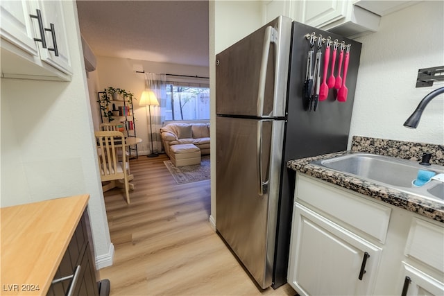 kitchen with light hardwood / wood-style floors, sink, dark stone counters, white cabinets, and stainless steel fridge