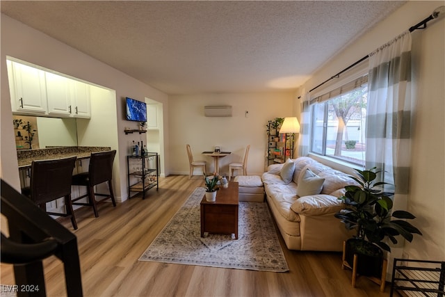 living room featuring a wall mounted AC, a textured ceiling, and light wood-type flooring