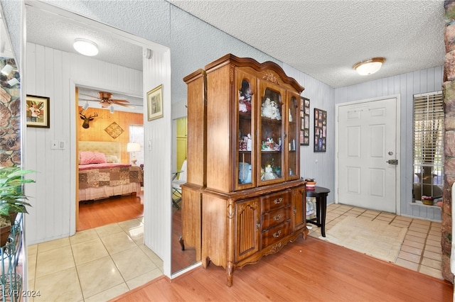 interior space with ceiling fan, wooden walls, light hardwood / wood-style flooring, and a textured ceiling