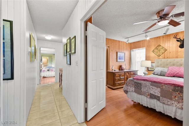 bedroom with wood walls, track lighting, ceiling fan, a textured ceiling, and light hardwood / wood-style flooring