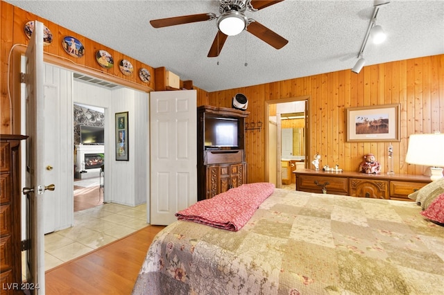 tiled bedroom with wood walls, a textured ceiling, ceiling fan, and ensuite bathroom