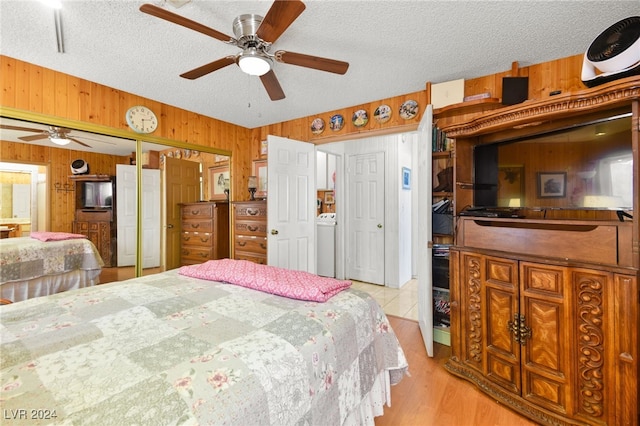 bedroom with wood walls, a textured ceiling, ceiling fan, light wood-type flooring, and washer / clothes dryer