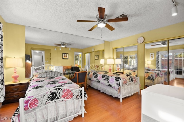 bedroom with two closets, hardwood / wood-style flooring, ceiling fan, and a textured ceiling