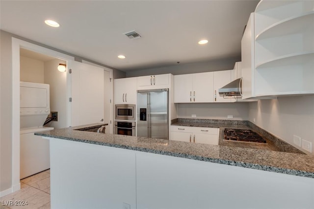 4525 Dean Martin Dr Unit 2704, Las Vegas, NV 89103 - kitchen featuring appliances with stainless steel finishes, estacked washer and dryer, wall chimney range hood, open shelves, and dark stone countertops