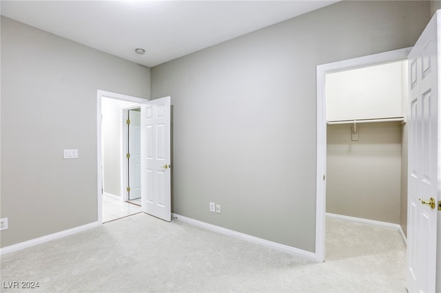 unfurnished bedroom with a spacious closet, light carpet, and a closet