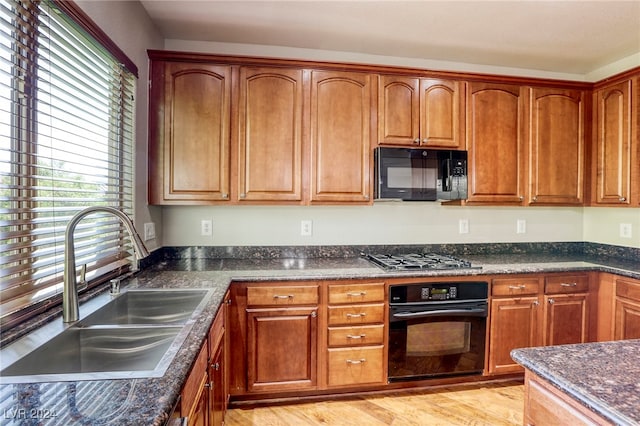 kitchen with light wood-type flooring, dark stone counters, sink, and black appliances