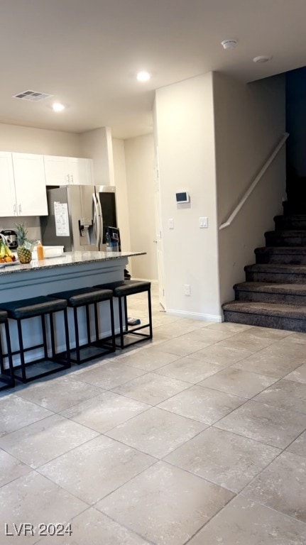 kitchen featuring light stone countertops, stainless steel fridge with ice dispenser, a breakfast bar, and white cabinets